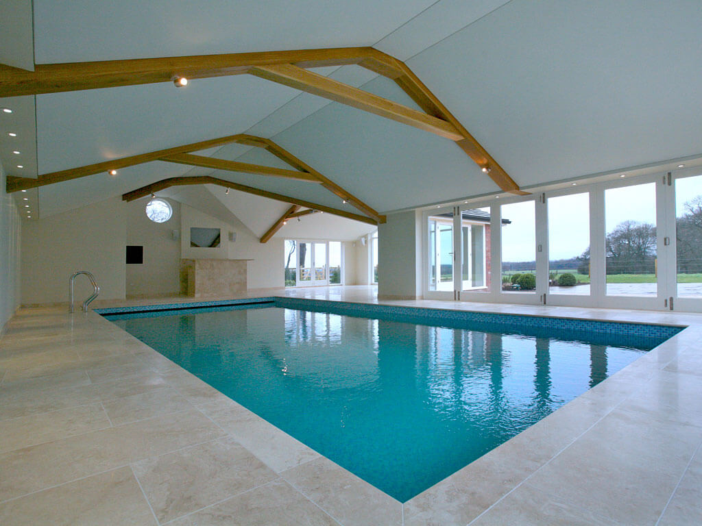 An indoor pool with blue tiles. There are exposed wooden beams above.