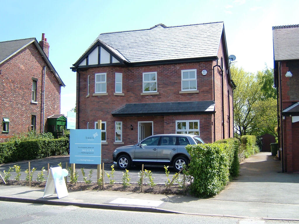 A modern house surrounded by two other houses. A car is parked in front of the house.