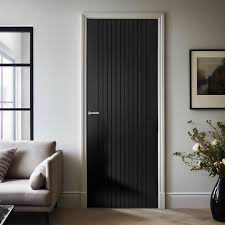a black door in a white wall. The door has a simple metal handle and has linear decoration